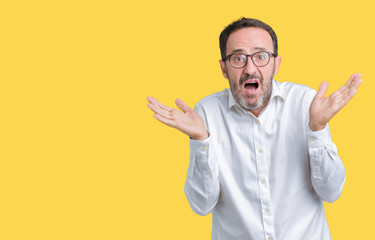 Handsome middle age elegant senior business man wearing glasses over isolated background clueless and confused expression with arms and hands raised. Doubt concept.