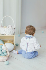 The child sits with his back on the floor next to a basket of Easter egg