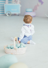 The child is sitting on the floor and next to it is a basket with Easter eggs