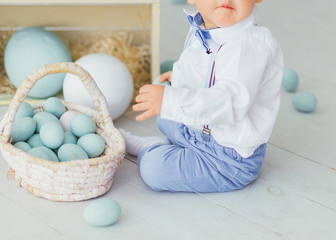 A child is sitting on the floor next to a basket of pastel blue Easter eggs