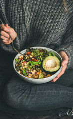 Healthy vegetarian dinner. Woman in jeans and warm woolen sweater holding bowl with fresh salad,...