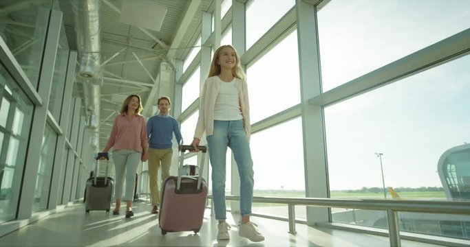 Caucasian teen cute and pretty girl walking the airport corridor with a suitcase on the wheels to the plane and her parents following.