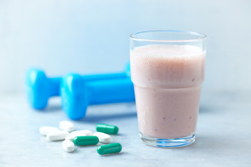Glass of Protein Shake with milk and raspberries. BCAA amino acids, L - Carnitine capsules and blue dumbbells in background. Sport nutrition. Stone / Wooden background. Copy space. 