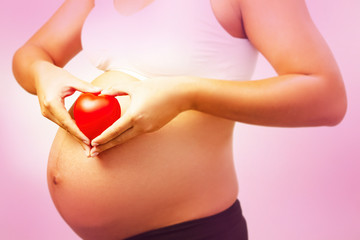 In selective focus of small red heart was holding by pregnant woman hands,sign and symbol of love and care