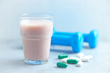 Glass of Protein Shake with milk and raspberries. BCAA amino acids, L - Carnitine capsules and blue dumbbells in background. Sport nutrition. Stone / Wooden background. Copy space. 