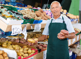 Senior male seller in apron putting fresh products on shelves in greengrocery
