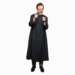 Middle age priest man wearing catholic robe pointing fingers to camera with happy and funny face....