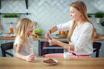 Mother and child daughter in home kitchen having fun drinking milk, healthy family lifestyle