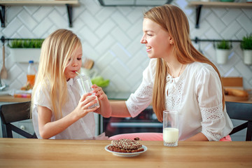 Mother and child daughter in home kitchen having fun drinking milk, healthy family lifestyle