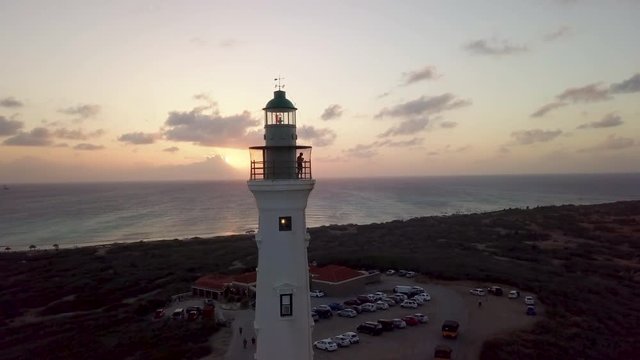 A man takes photos of Aruba from the top of the California Lighthouse during a beautiful orange sunset. Aerial static.