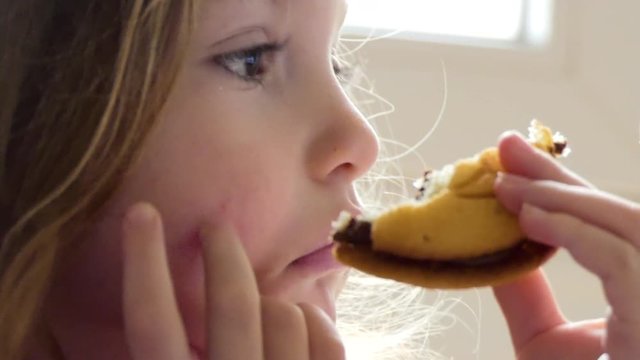 A young girl holding a half-eaten cookie stares at a TV screen.