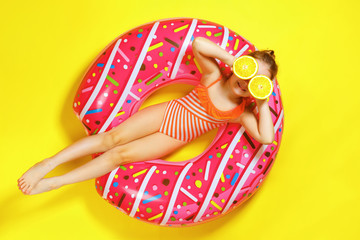 A little child girl in a swimwear suit lying on a donut inflatable circle. Yellow background. Top view. Summer concept.