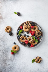 Homemade cinnamon and chocolate mini donuts on the plate with berries and mint on the light grey backgorund