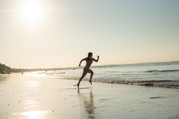 Woman runs barefoot on the beach at sunset. Silhouette of a woman by the sea at sunrise