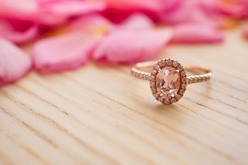 Jewelry pink diamond ring on wood table with beautiful rose petal background close up