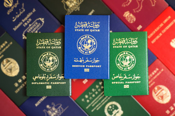 Multicolored different passports of the State of Qatar on a blurred background of various documents of many countries of the world