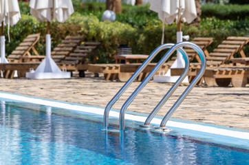 handrails by the pool with blue water against the sun loungers and folded umbrellas
