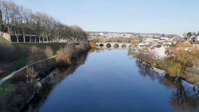 View of the Vienne river, in the city of Limoges, central west France. In the background there is an old medieval bridge called "Le Pont Saint Etienne" in french. Sunny day, blue sky.