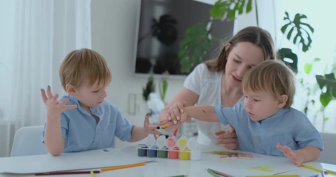 Two children of boys and mother are engaged in creative development doing homework by fingering on paper. The development of tactile sensations and small mathematics.