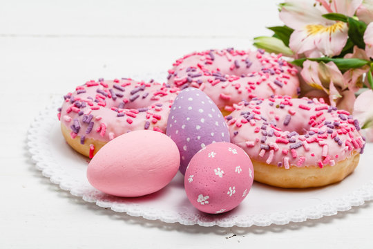 stylish easter donuts and painted eggs on rustic wooden background top view with candle yellow flowers