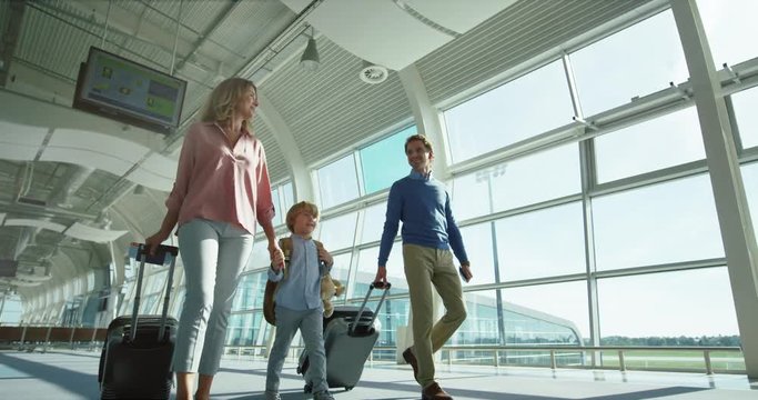 Caucasian parents with small nice son and big suitcases on wheels passing through the camera in the airport passage while going to the departure or arrival gates.