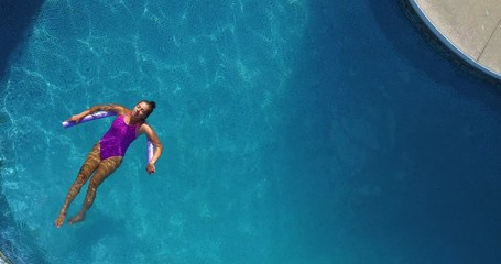 Young girl relaxing on a noodle in a large backyard swimming pool.