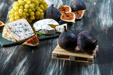 Cheese plate served with grapes, figs and nuts on a black background. Food background. Top view. Copy space