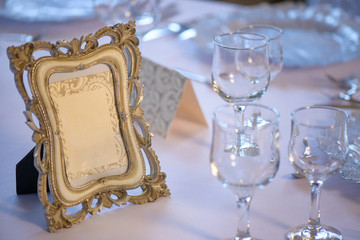 Distressed embellished wooden picture frame with copy space positioned on a table prepared for a special event, with clean drinking glasses for water and wine, decorated plates and silverware 