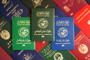 Multicolored different passports of the State of Qatar on a blurred background of various documents of many countries of the world