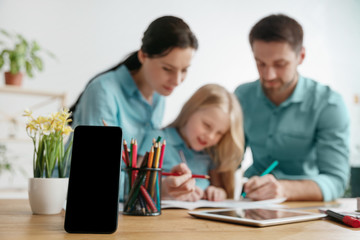 Father, mother and their daughter are smiling while spending time together. A day with family. Smartphone on the front is the mock up for your advertisement. Education, studying and knowledge sharing