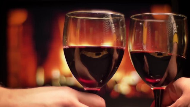 Closeup shoot of two hands clinking glasseswith red wine celebrating a night date with cozy warm fireplace on the background indoors in the evening