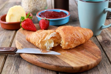 croissant with strawberry jam, fresh strawberries and a coffee on wooden table