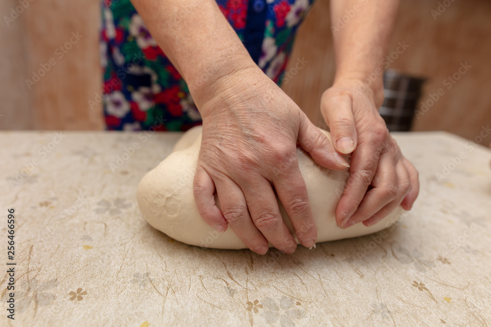 Wall mural Woman kneads dough with hands in the kitchen