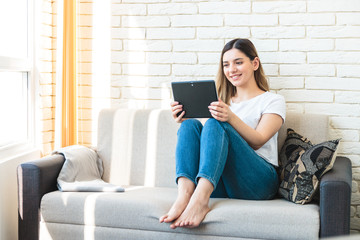 Obraz premium Attractive young woman using a digital tablet while relaxing on a sofa at home