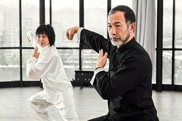 Couple of senior masters practicing qi qong taijiquan at studio. Breathing exercise and martial art moves, traditional chinese qi energy management gymnastics.
