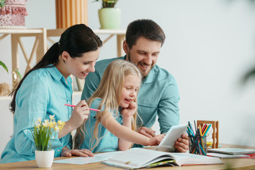 Father, mother and their daughter are smiling while spending time together. A day with family. Young happy couple with child are studying with the tablet. Education, studying and knowledge sharing