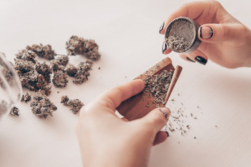Close up of marijuana blunt with grinder. Cannabis use concept. Woman preparing and rolling...