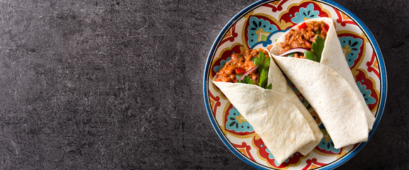 Typical Mexican burrito wrap with beef, frijoles and vegetables on black background. Top view. Copyspace. Panoramic view