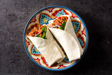 Typical Mexican burrito wrap with beef, frijoles and vegetables on black background. Top view. Copyspace - obrazy, fototapety, plakaty