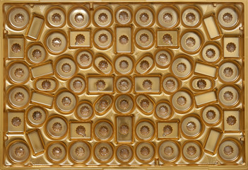 Inside of chocolate box gift, shiny gold plastic background with small empty compartments.