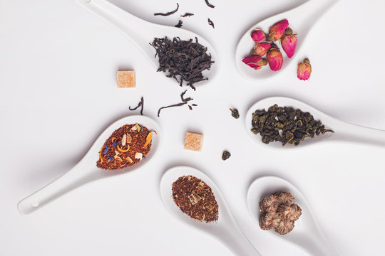 Different variety of dry tea in white spoons on the white background