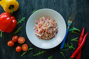 Delicate salad of white cabbage, carrots and bell peppers. Decorated with greens and vegetables. Veggie dish. Proper nutrition. Dark wooden background.