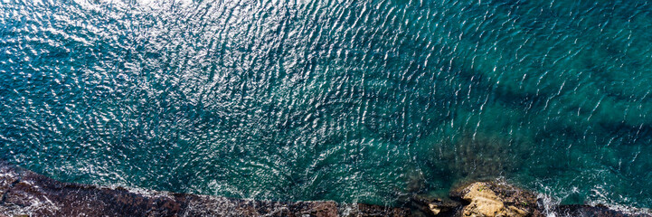 Aerial top view of sea waves hitting rocks on the shore with turquoise sea water