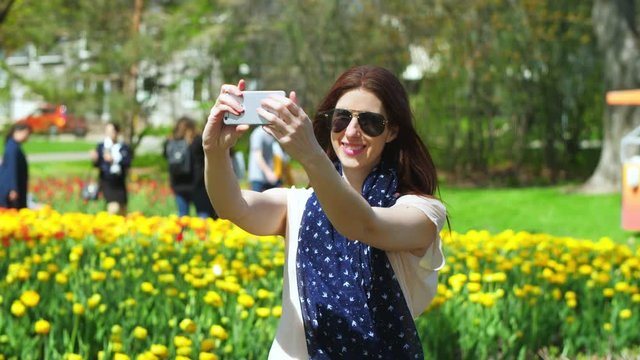 Attractive woman takes selfies in front of colorful flowers