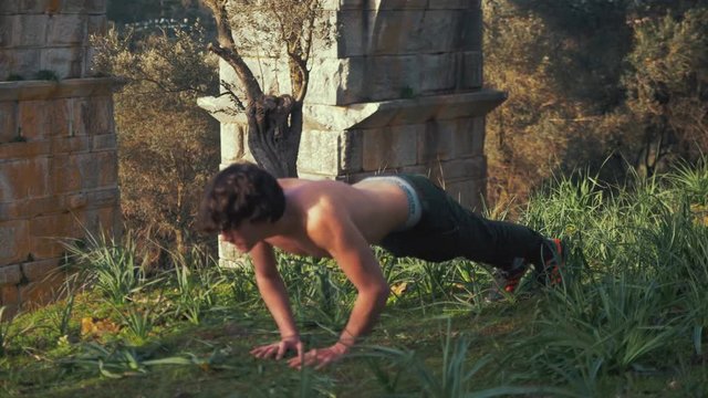 Young strong lean fit man does diamond push ups within nature