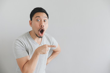 Wow and surprised face of man in grey t-shirt with hand point on empty space.