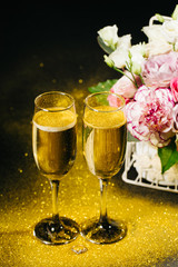 Bouquet with beautiful roses and glasses of champagne on black background with gold 