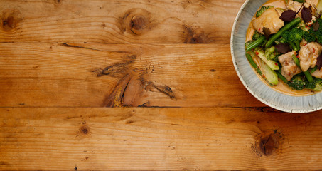 A bowl of succulent Thai Red Chicken Curry shot a wooden background in a banner format