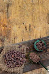 Fototapeta na wymiar Cacao beans, cacao powder and chocolate on a piece of burlap on old plank over a wooden background