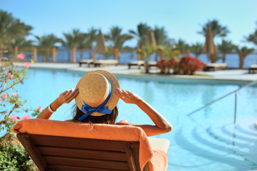 Young beautiful woman Sitting On Sun Loungers By Swimming Pool at the hotel in hat